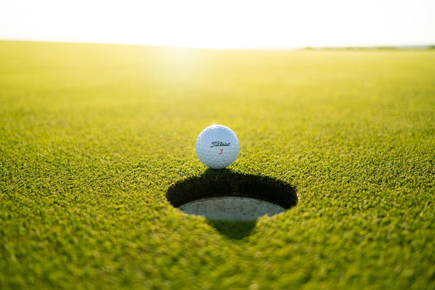 Golf ball resting on the lip of the cup